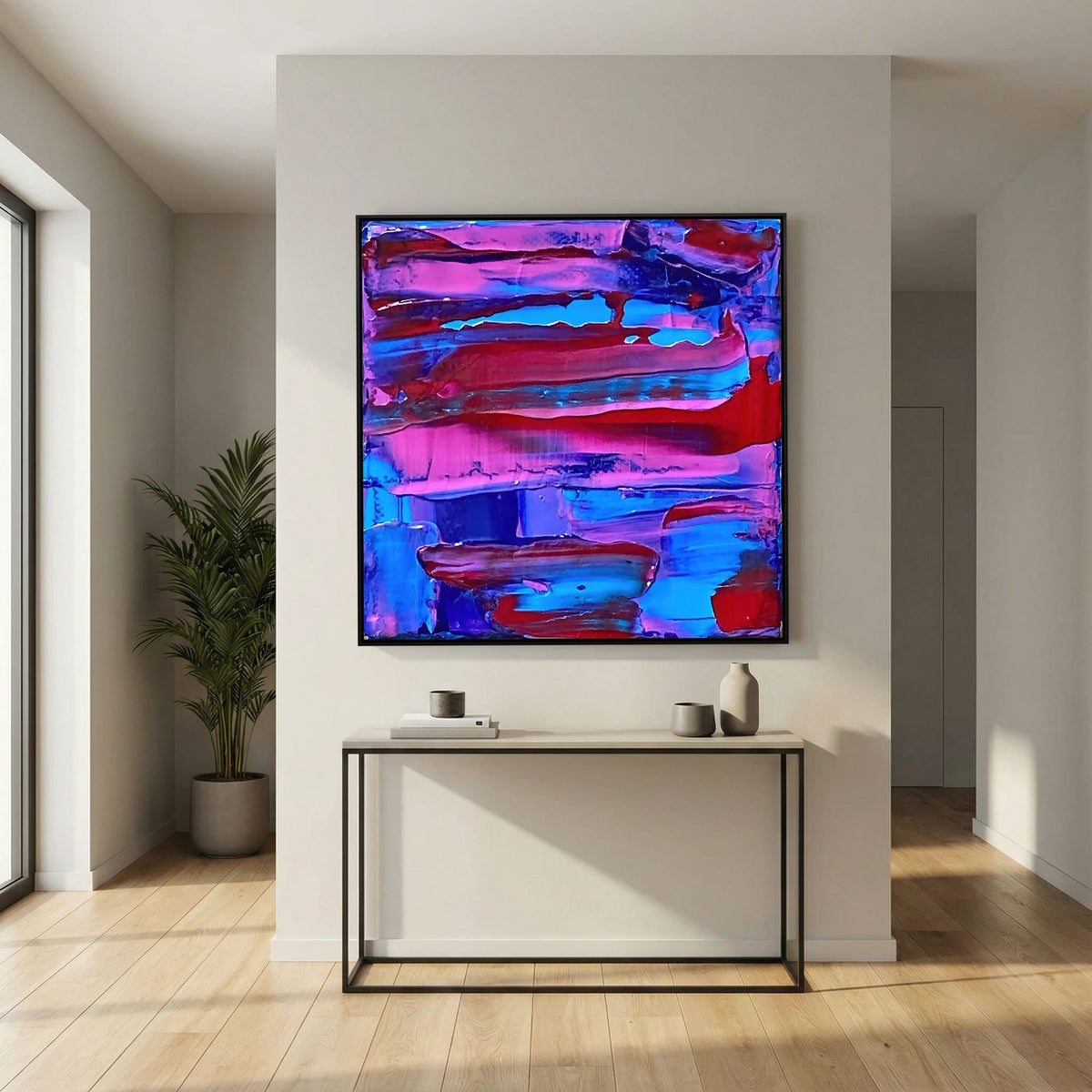 Roze, rood en blauw abstract werk Sunset Overflow van Tim Hupkes in een zwarte lijst boven een smalle sidetable in een hal