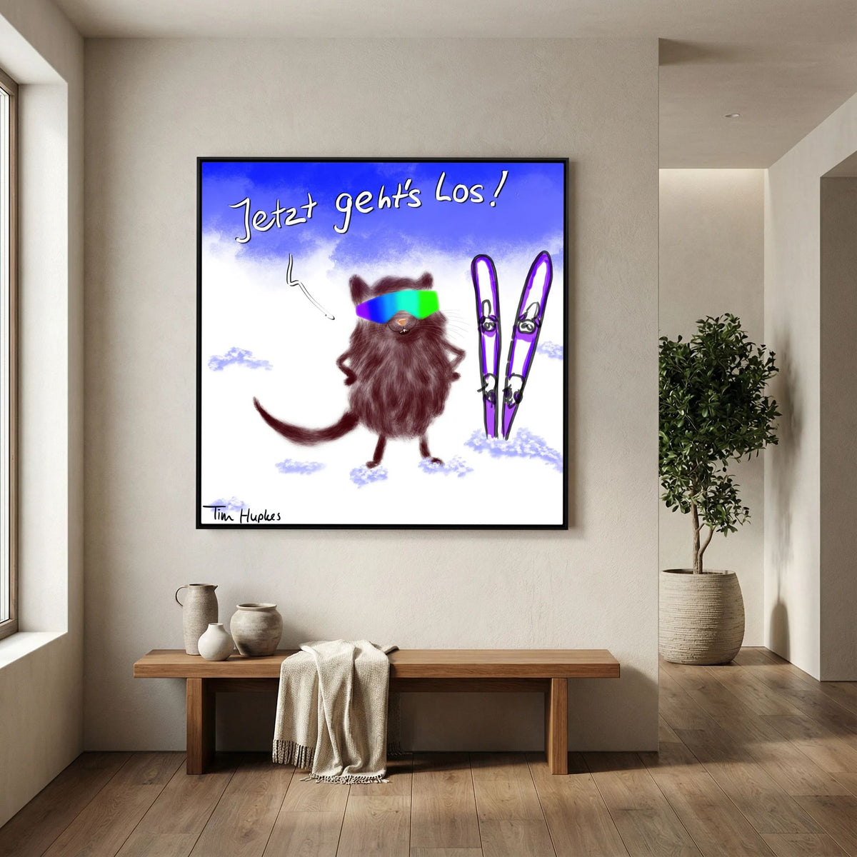 Black-framed Jetzt Geht's Los by Tim Hupkes hanging above a wooden bench in a bright hallway, showing a furry skier in goggles