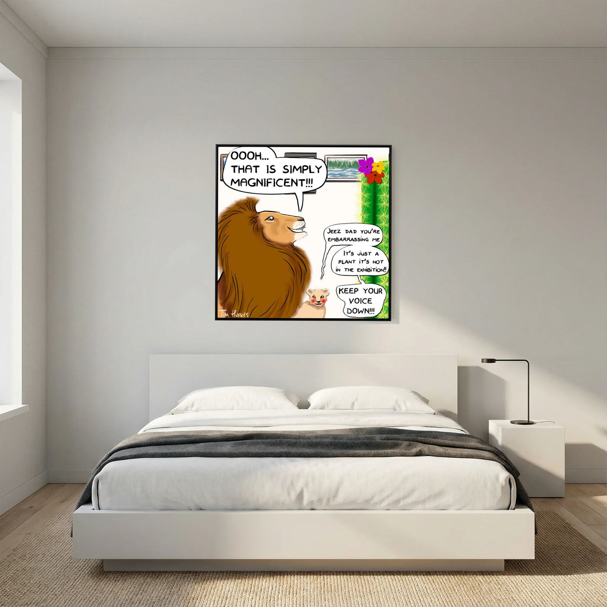 Faux Pas by Tim Hupkes cartoon of a lion admiring a cactus, black frame, hung above a low white bed in a minimalist bedroom