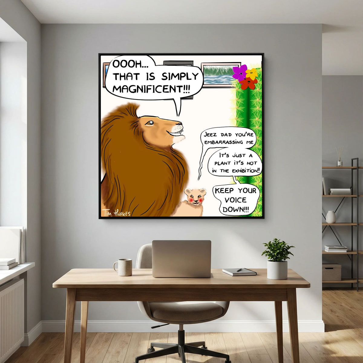 Faux Pas by Tim Hupkes lion cartoon in a black frame hanging above a wooden desk with a laptop in a home office