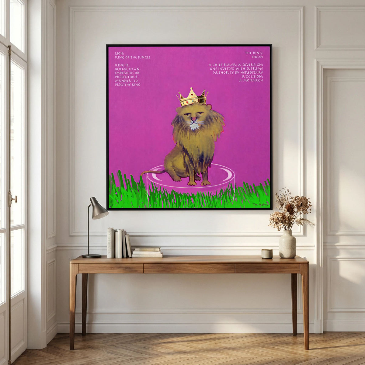 Black-framed The King by Tim Hupkes with its crowned lion on pink, hanging above a wooden console table in a panelled room