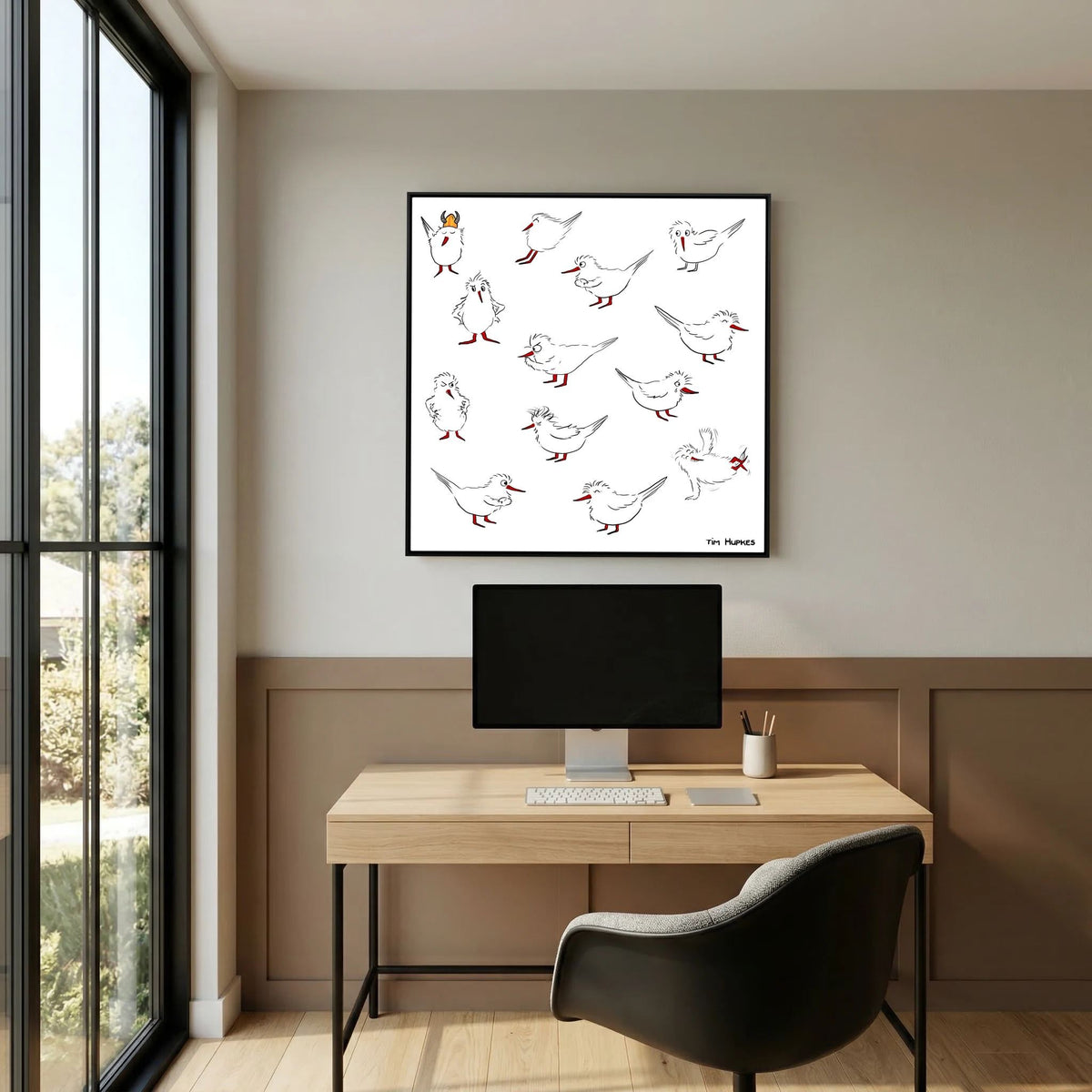 Black-framed Blackburn & Haptoe - everyday heroes by Tim Hupkes hanging above a light wood desk with a monitor in a home office