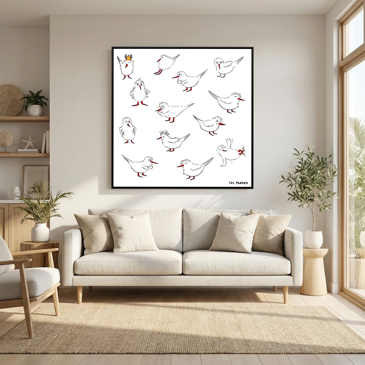 Black-framed Blackburn & Haptoe - everyday heroes by Tim Hupkes above a white sofa with cushions in a sunny living room with a rug