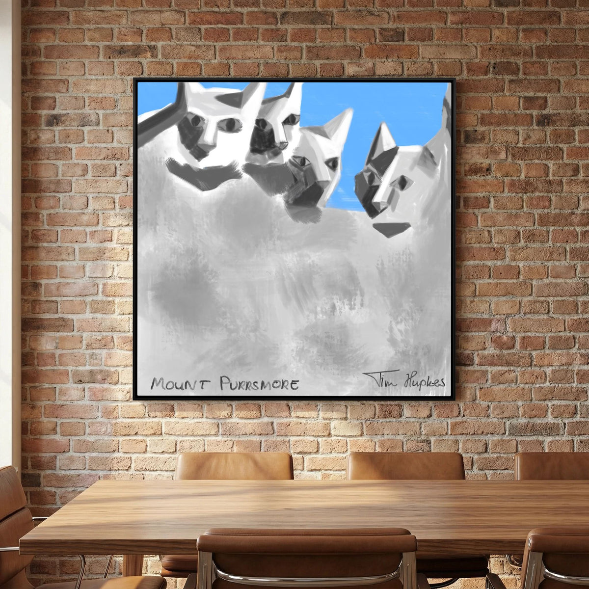Mount Purrsmore by Tim Hupkes canvas print in a black frame on an exposed brick wall above a wooden table and brown leather chairs
